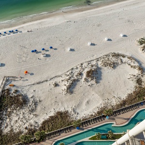 Experience breathtaking beachfront views from this balcony, overlooking the sandy shore and inviting pool area below