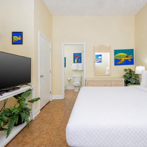 Brightly colored artwork complements the guest bedroom featuring a queen bed, flat-screen TV, and a glimpse of the bathroom