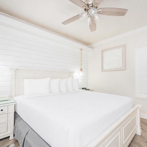 Serene bedroom features a plush king bed adorned with decorative pillows, soft lighting, and a cozy chair by the window