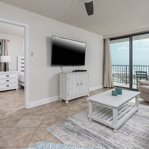 The living area features a large TV, stylish decor, and stunning beachfront views through expansive glass doors
