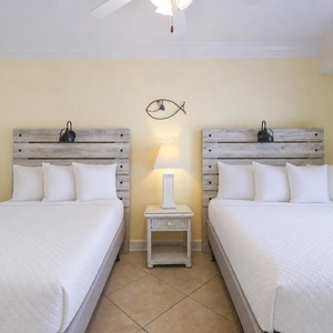 Two cozy double beds with white linens and wooden headboards create a welcoming atmosphere in this vibrant guest room