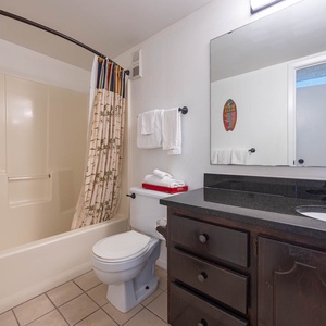 This bathroom features a clean design with a shower/tub combo, dark cabinetry, and fresh towels for a refreshing stay