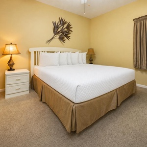A cozy bedroom features a king bed, a bedside lamp, and warm yellow walls creating a welcoming atmosphere