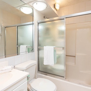 The bathroom features clean white tiles, ample lighting, and a glass shower, perfect for a refreshing retreat