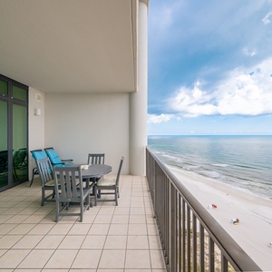 Relax on the spacious balcony with vibrant blue chairs, overlooking the tranquil shoreline and inviting beach activities