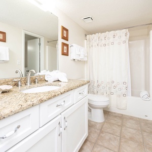 Guest bathroom featuring a granite countertop, ample towels, and a tub/shower combo with a decorative shower curtain