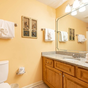 Warm yellow walls complement the wooden cabinetry and neatly arranged towels in this inviting guest bathroom space