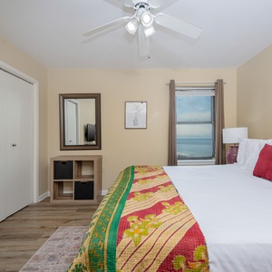 This inviting guest bedroom features a king bed with a colorful quilt, a mirror, and a window showcasing a beach front view