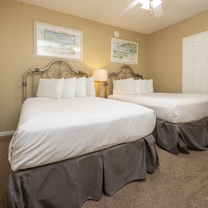Rest in this inviting guest room featuring two double beds, soft lighting, and charming coastal artwork on the walls