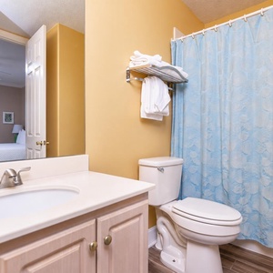 The guest bathroom features a bright yellow wall, a blue shower curtain, and a convenient view into the adjacent bedroom