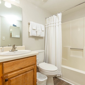 Bright and inviting guest bathroom featuring a clean tub/shower combo and warm wooden cabinetry for a cozy retreat