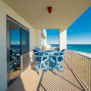 Balcony features blue Adirondack chairs and a table, offering a serene view of the gulf and the white sand beach below
