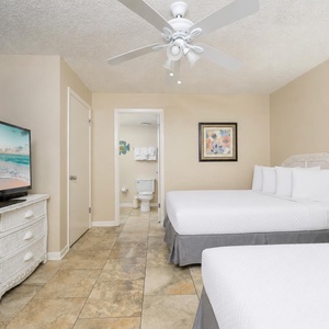 Guest bedroom featuring two double beds, a large TV, and an en-suite bathroom, with decorative accents and a ceiling fan
