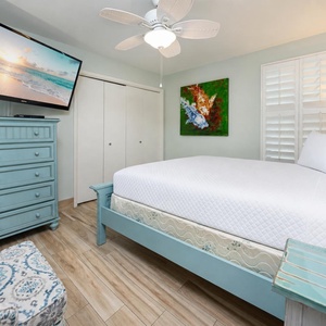 Guest bedroom featuring a cozy queen bed, stylish blue dresser, and a large TV for entertainment