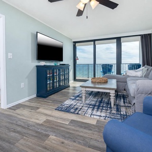 This living area features a large TV, a cozy seating arrangement, and stunning beach front views through expansive windows