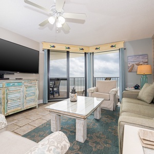 Cozy living area features a large TV, comfortable seating, and a balcony with views of the beach and Gulf
