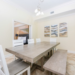 This dining area features a wooden table with white chairs and beautiful coastal artwork, creating a welcoming atmosphere