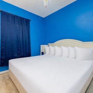 The master bedroom features a bright blue accent wall, a king bed with plush pillows, and a cozy atmosphere for relaxation