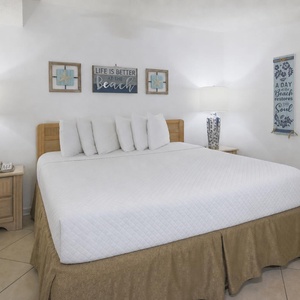 A bright bedroom features a king bed with plush pillows, stylish lamps, and beach decor, creating a relaxing atmosphere