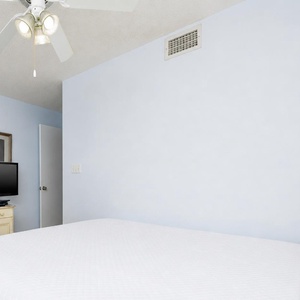 Cozy guest bedroom features a king bed, a ceiling fan, and a TV on a light-colored dresser against soft blue walls
