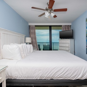 This bedroom features a king-sized bed, a colorful abstract painting, and a TV, with a stunning beachfront view