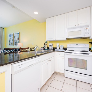 This kitchen features bright yellow walls, sleek granite countertops, and a view of the beach through large windows