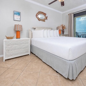 Cozy master bedroom features a king bed with white linens, colorful lamps, and direct access to a balcony with gulf views