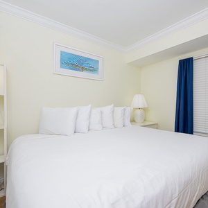 The master bedroom features a plush bed, soft lighting, and a charming beach-themed artwork, perfect for relaxation