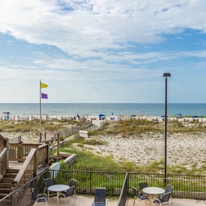 This inviting outdoor space features a view of the beach, perfect for relaxing with friends by the tables and chairs