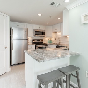 A sleek kitchen features stainless appliances, a granite countertop, and a cozy bar area with two stools for casual dining