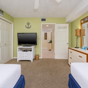 Bright guest bedroom featuring a full and a twin bed, a large TV, and cheerful beach decor against a refreshing green wall