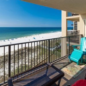 A turquoise rocking chair and wicker furniture create a relaxing balcony space overlooking the beach and gentle waves