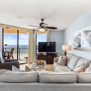 The living room features a spacious gray sectional sofa with queen sleeper, a large TV, and a view of the beach