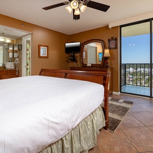 The cozy master bedroom features a queen bed, a charming armchair, and the balcony with a view of the surrounding area