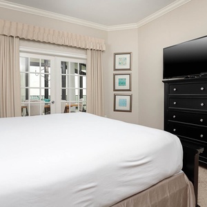 The master bedroom features a large king bed, a TV for entertainment, and views through glass doors leading to a dining area