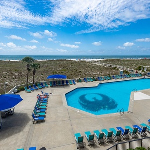 Expansive pool area with vibrant loungers overlooks the beach, inviting relaxation under the sunny sky and gentle gulf breeze