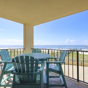 The balcony features a round table with turquoise chairs, offering a view of the beach and the pool area
