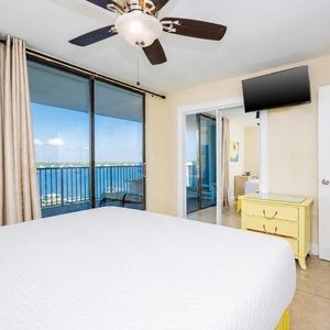 King master suite featuring a yellow dresser, a TV, and a stunning view of the water from the large glass doors