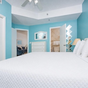 Bright turquoise walls complement a spacious bedroom featuring a plush king bed, dresser, and adjoining bathroom