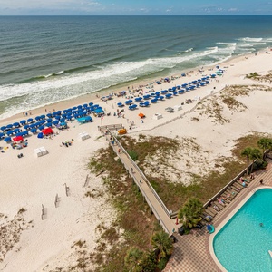 This stunning view showcases the beach with vibrant blue umbrellas and the sparkling pool and lazy river below