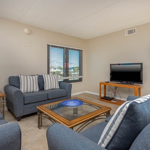 The living area features comfortable seating, a TV, and a view of the vibrant surroundings through large windows