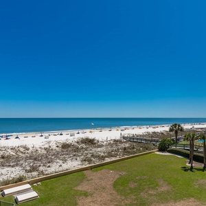 The view showcases a pristine beach with white sand and colorful umbrellas, framed by a clear blue sky and lush greenery