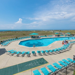 Inviting pool area features turquoise loungers and a shaded cabana, with a scenic view of the beach in the background