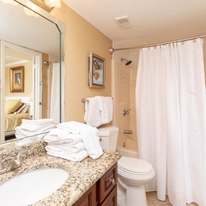 Bright bathroom featuring a granite countertop, neatly arranged towels, and a tub/shower combo with a shower curtain