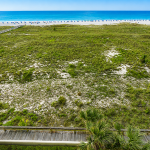 Expansive view of the beach with lounge chairs lining the shore, complemented by a pool area and lush greenery below