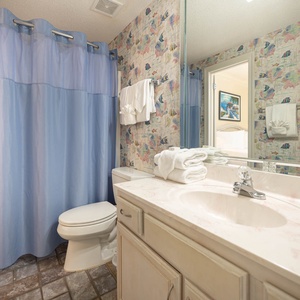 Brightly decorated full bathroom featuring a tub/shower combo, plush towels, and a colorful fish-themed wallpaper