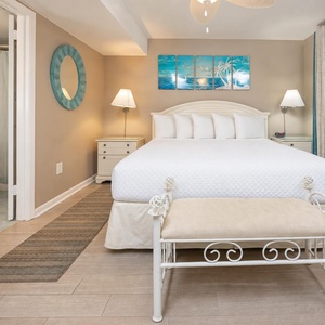 Cozy bedroom featuring a large king bed, decorative art, and a stylish bench, perfect for relaxing after a beach day