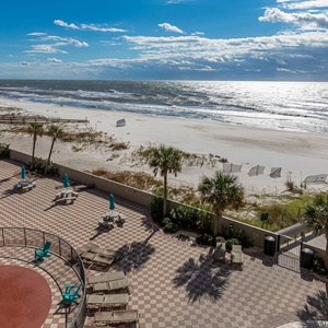 This balcony overlooks a beachfront setting with palm trees, lounge chairs, and a vibrant pool and lazy river area