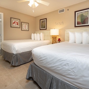 Guest bedroom featuring two queen beds with plush white bedding, decorative art, and a cozy lamp, creating a welcoming vibe