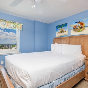 This bedroom features a comfortable bed, vibrant beach-themed artwork, and a scenic view from the window
